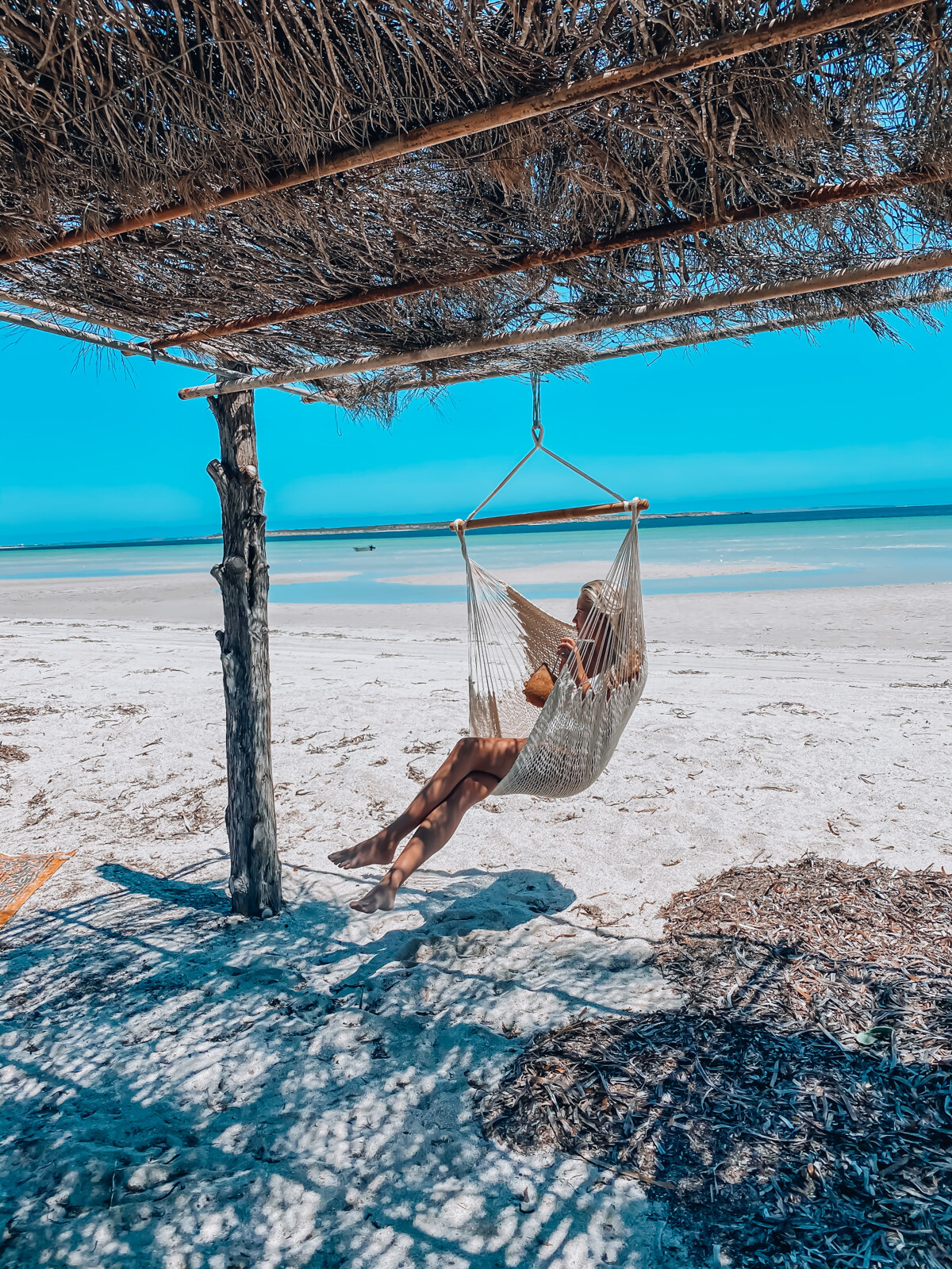 A woman relaxes in a chair hammock on a beach in Streaky Bay